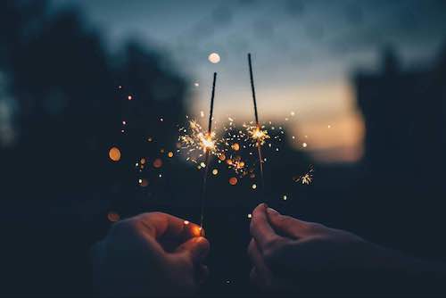 Two hands holding sparklers with a nightly blurry background