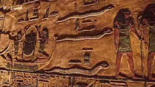 Ancient Egyptian carvings showing hieroglyphics, figures, and serpents on a sandstone wall.