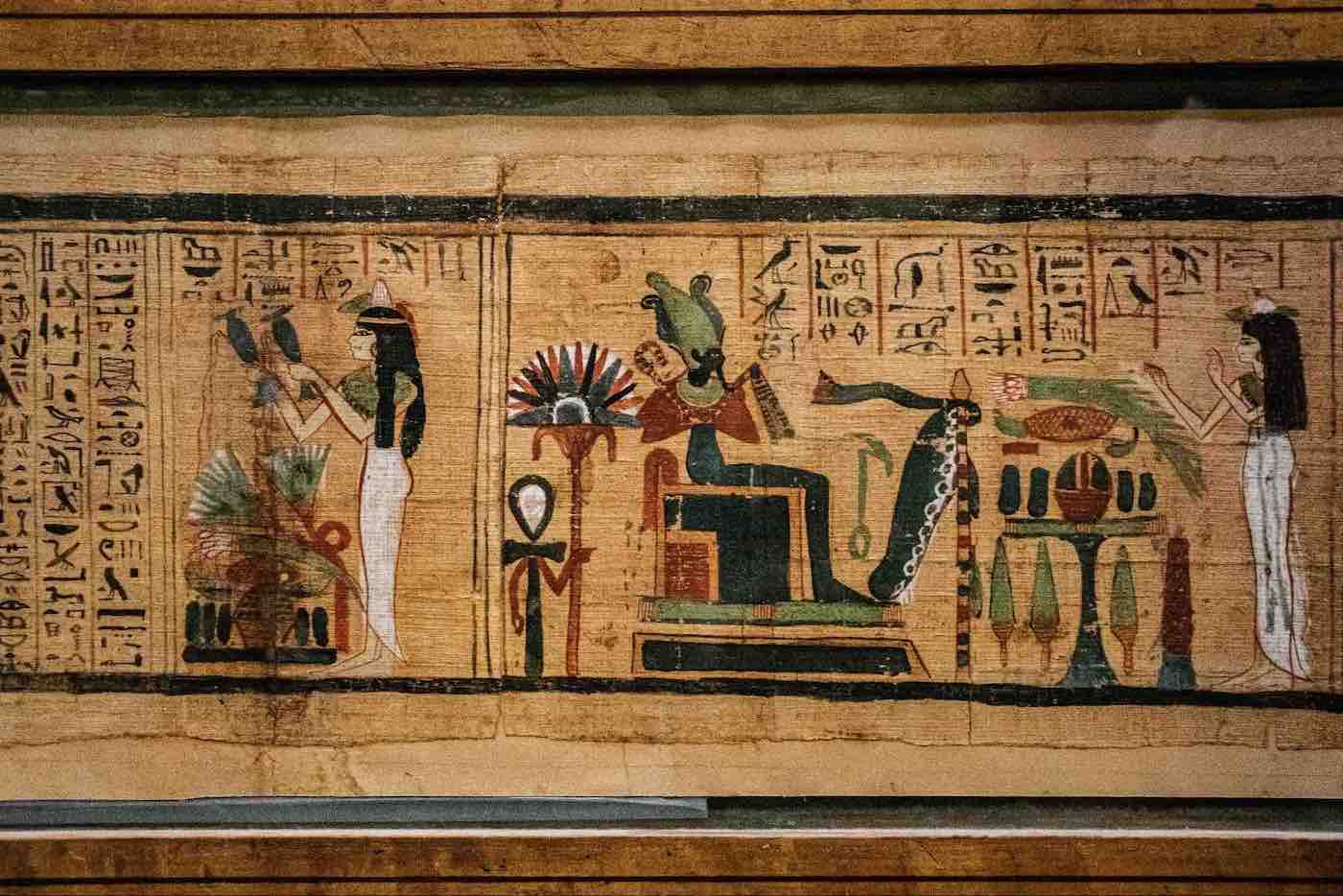 Ancient Egyptian papyrus showing hieroglyphs and colorful depictions of deities and figures in ceremonial scenes.