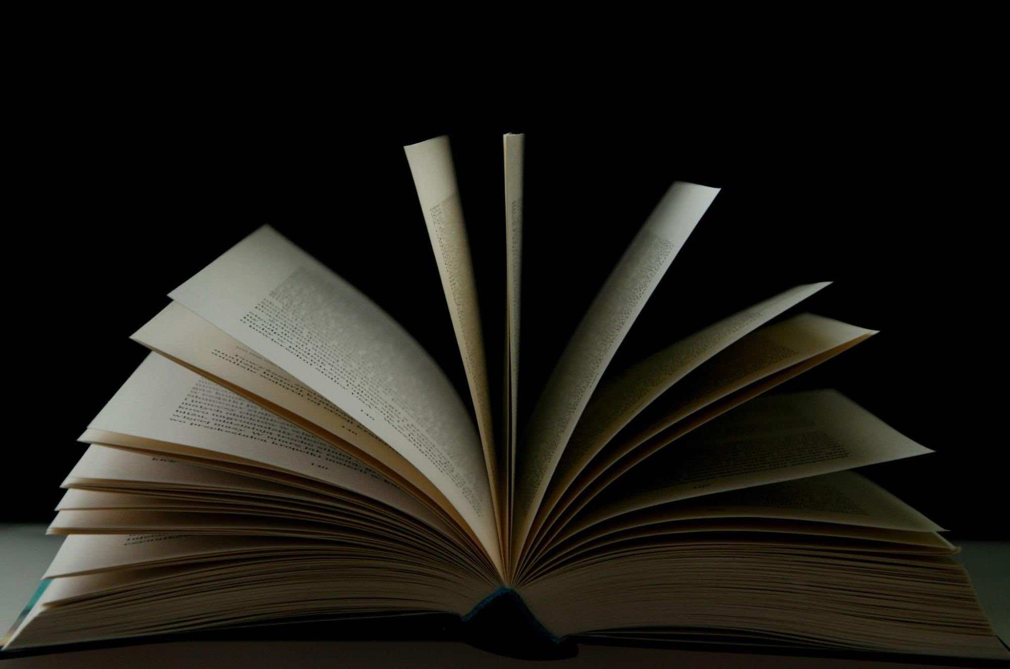 Open book with fanned pages against a dark background, symbolizing knowledge, literature, and storytelling.