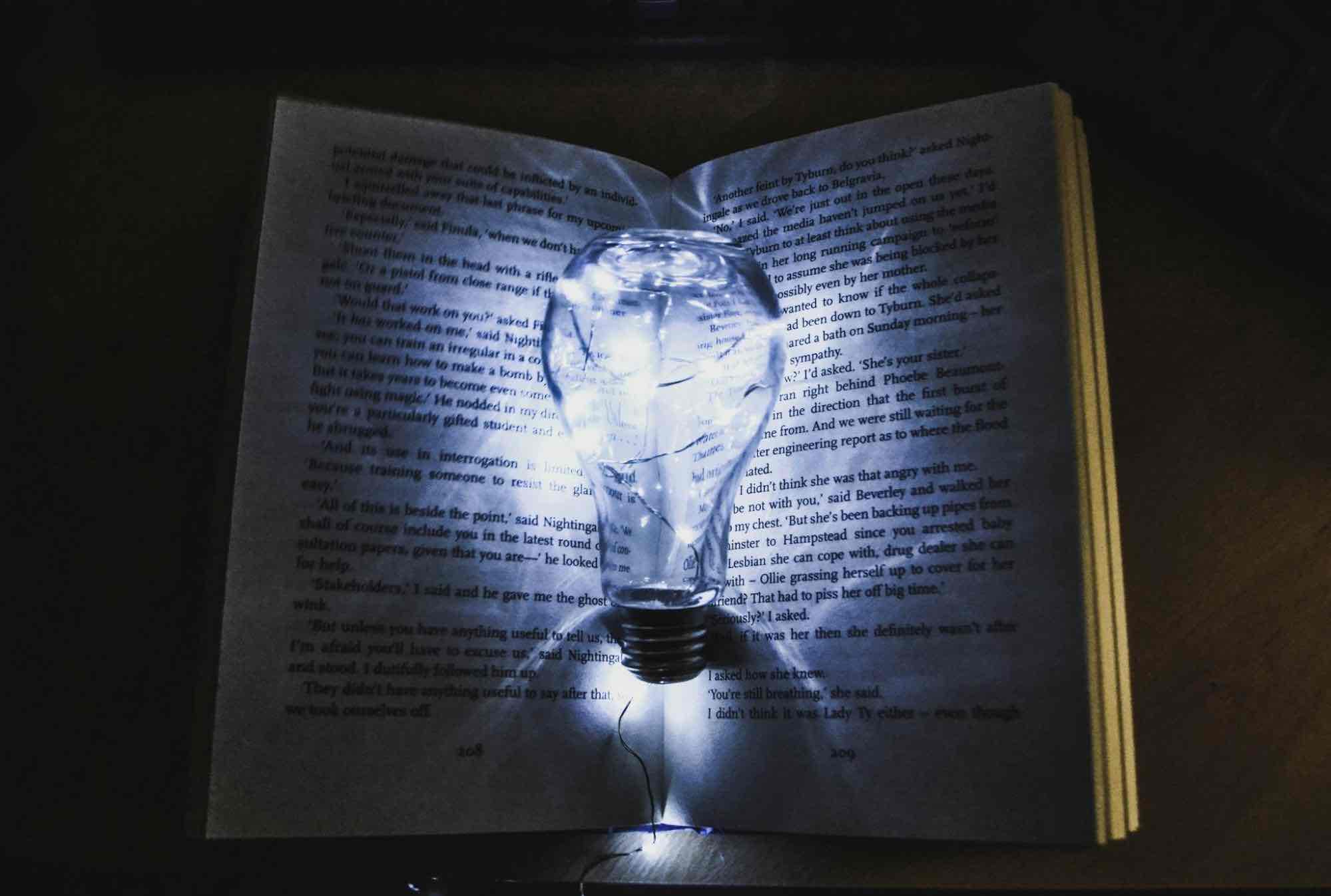 Glowing light bulb placed on an open book in a dim lit room.