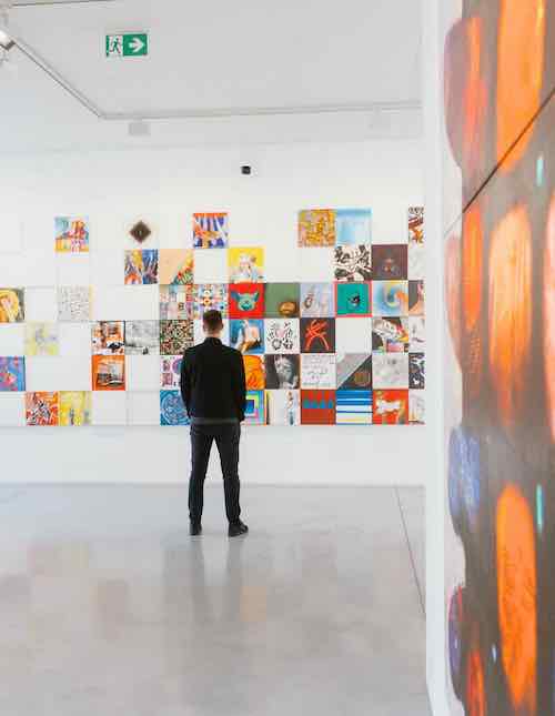 Man standing in front of a colorful modern art exhibit, observing diverse artistic works displayed on a gallery wall.